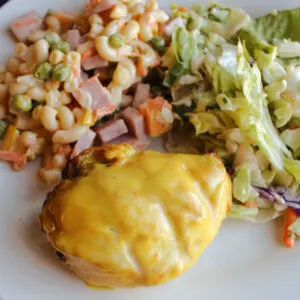 Close up of a grilled yellow chicken breast with mustard ranch sauce served with sweet macaroni salad and a green salad.
