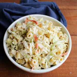 Serving bowl filled with coleslaw macaroni salad with a creamy dressing, shredded carrots and cabbage, and cooked pasta, ready to be served.