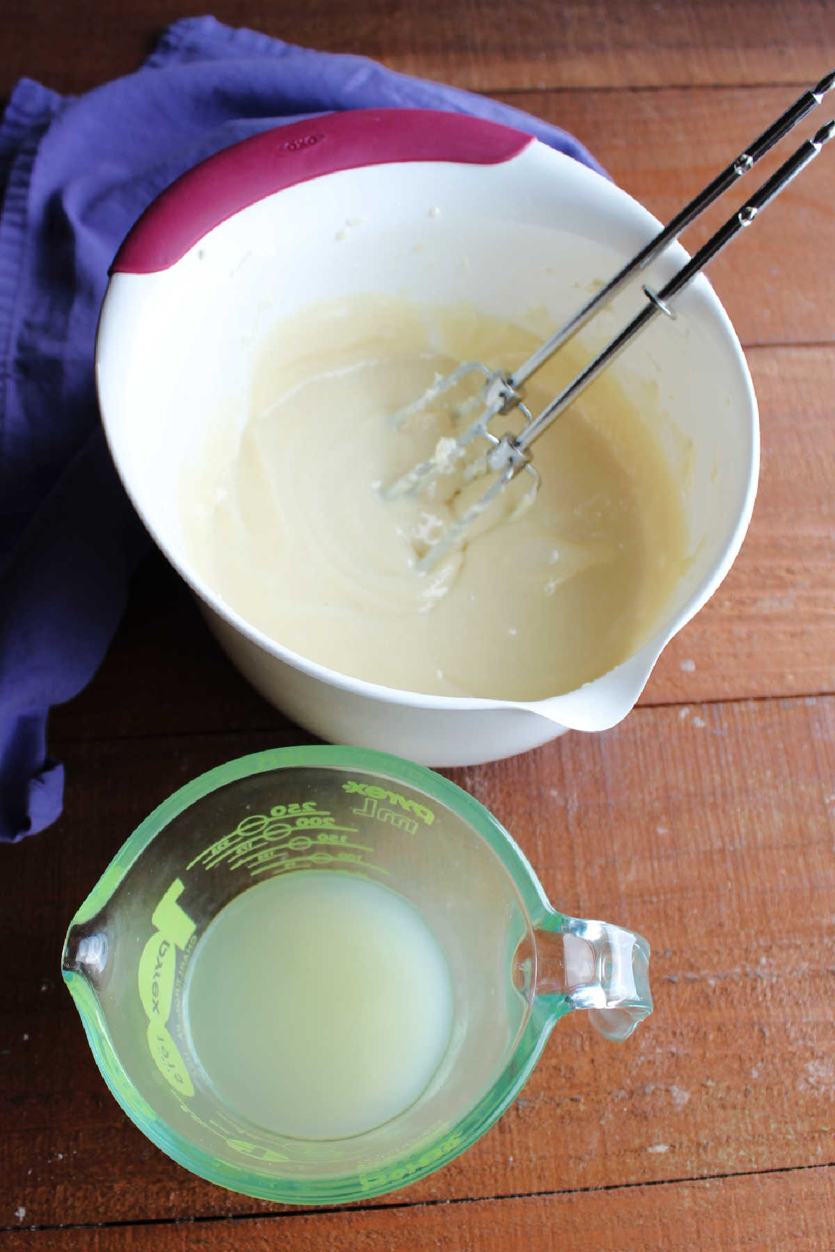 Mixing bowl containing smooth cream cheese and condensed milk mixture next to a measuring cup with lemon juice inside.