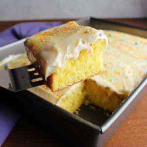 Spatula lifting out piece of lemon cake topped with lemon cream cheese frosting and sprinkles.