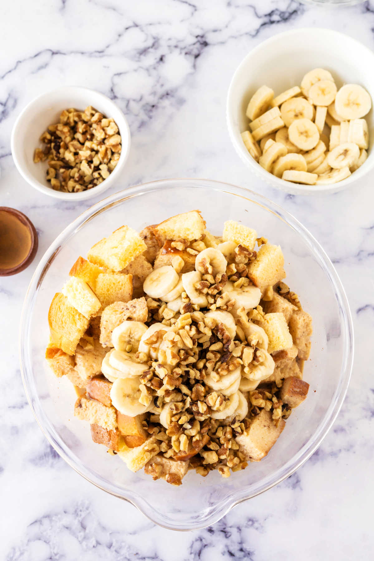 Bowl of bread cubes with sliced bananas, walnuts, and custard.