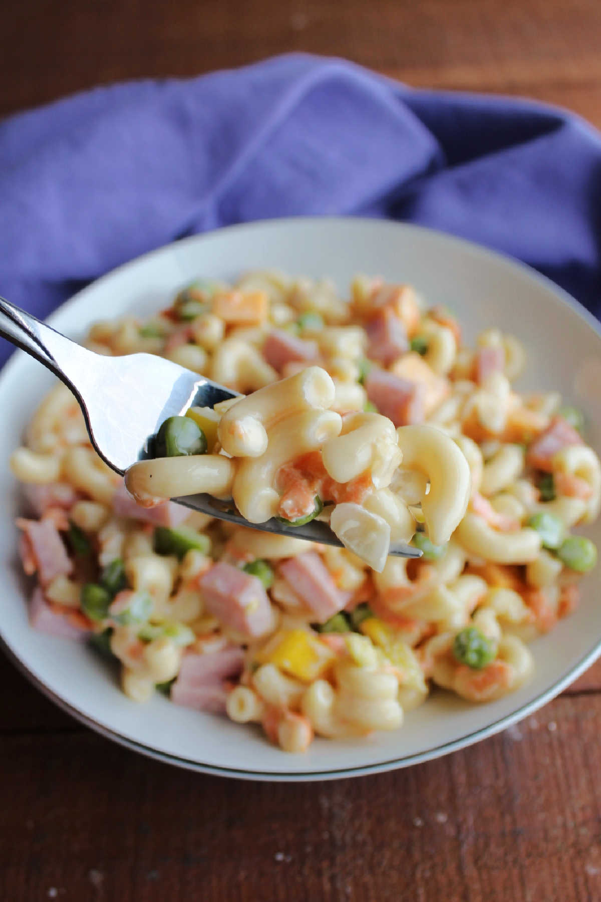 Bite of sweet macaroni salad on fork showing peas, onion, and shredded carrots. 