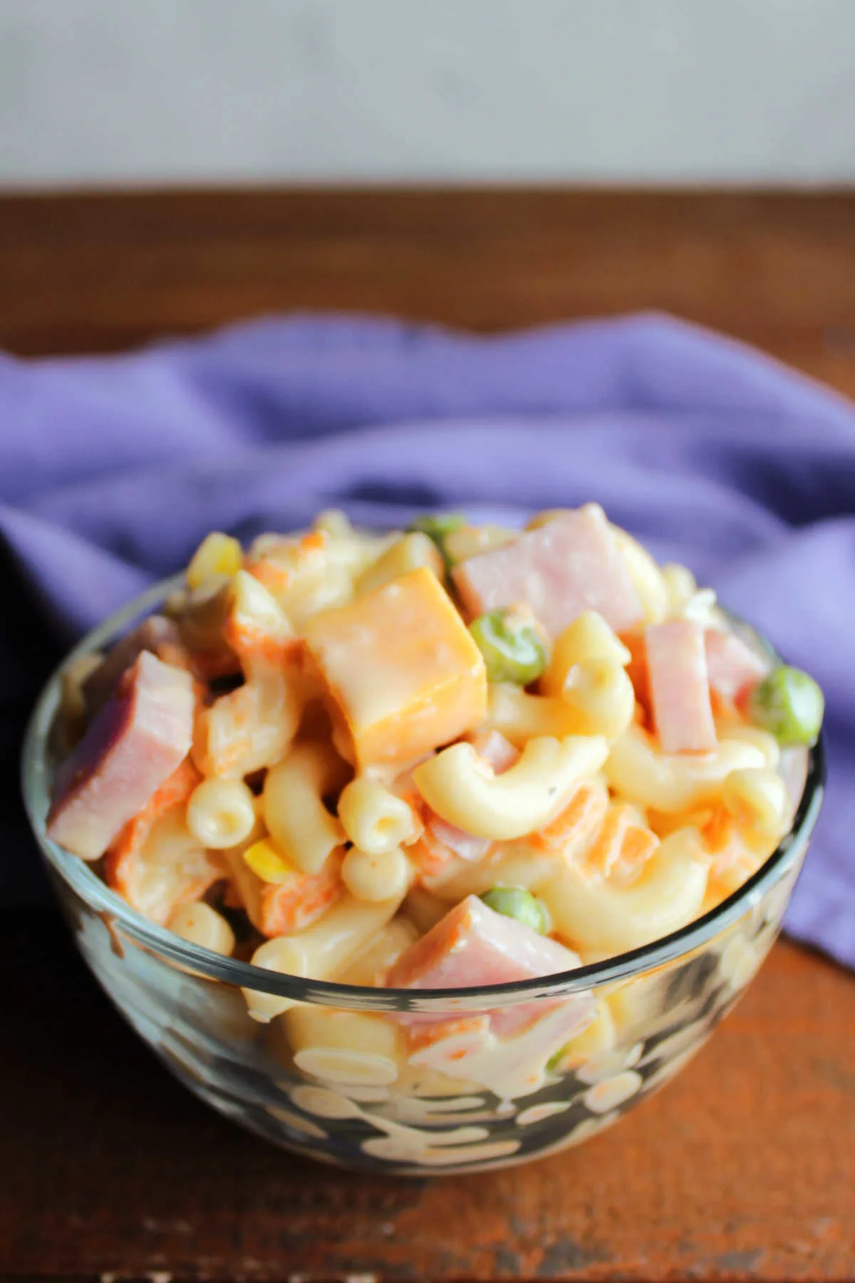 Small glass bowl filled with creamy sweet macaroni salad with cheese and ham. 
