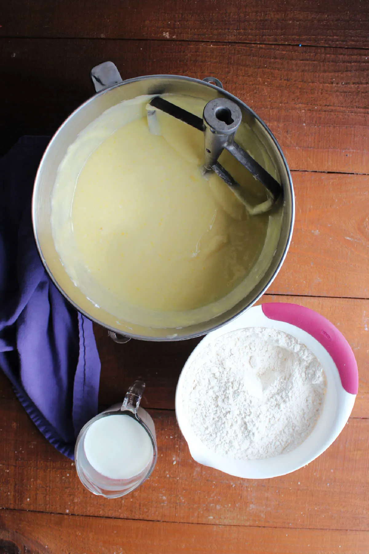 Mixer bowl with butter, sugar, oil, egg mixture next to bowl with dry ingredients and a measuring cup with milk ready to be made into vanilla cake batter.