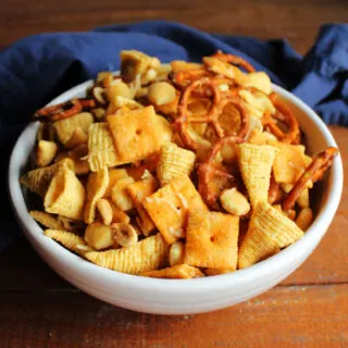 Serving bowl filled with snack mix featuring cheese crackers, bugles, peanuts, pretzels and oyster crackers coated in ranch mixture with bits of Parmesan cheese melted on it.