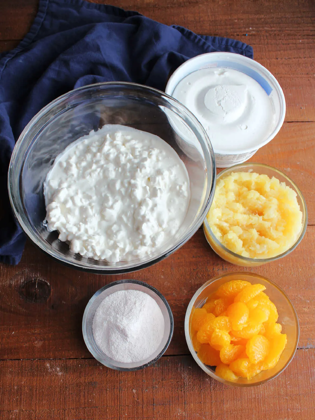 Ingredients including mandarin oranges, orange jello powder, crushed pineapple, cottage cheese, and whipped topping ready to be made into jello salad.
