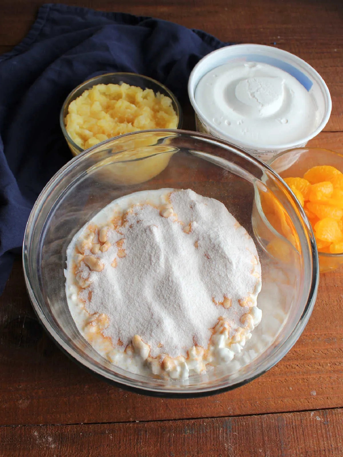 Orange Jello powder sprinkled over bowl of cottage cheese with other ingredients nearby. 