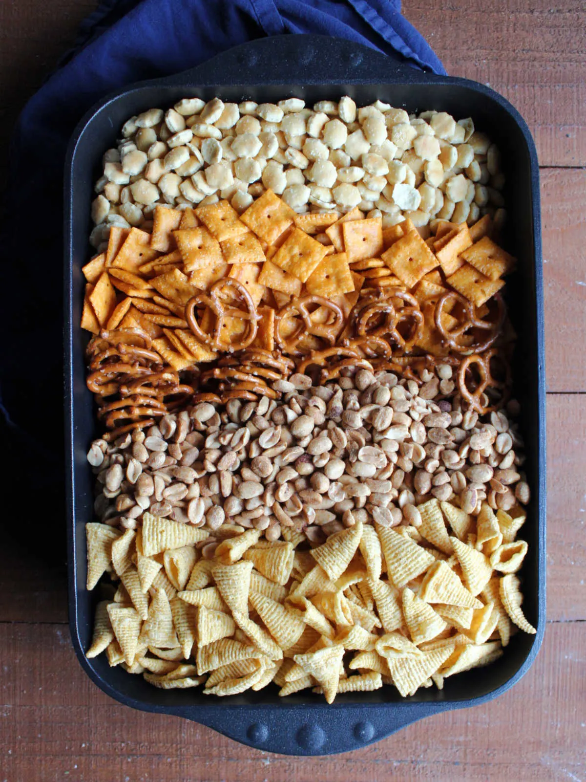 Large roasting pan filled with oyster crackers, cheese crackers, pretzel twists, peanuts, and bugles.