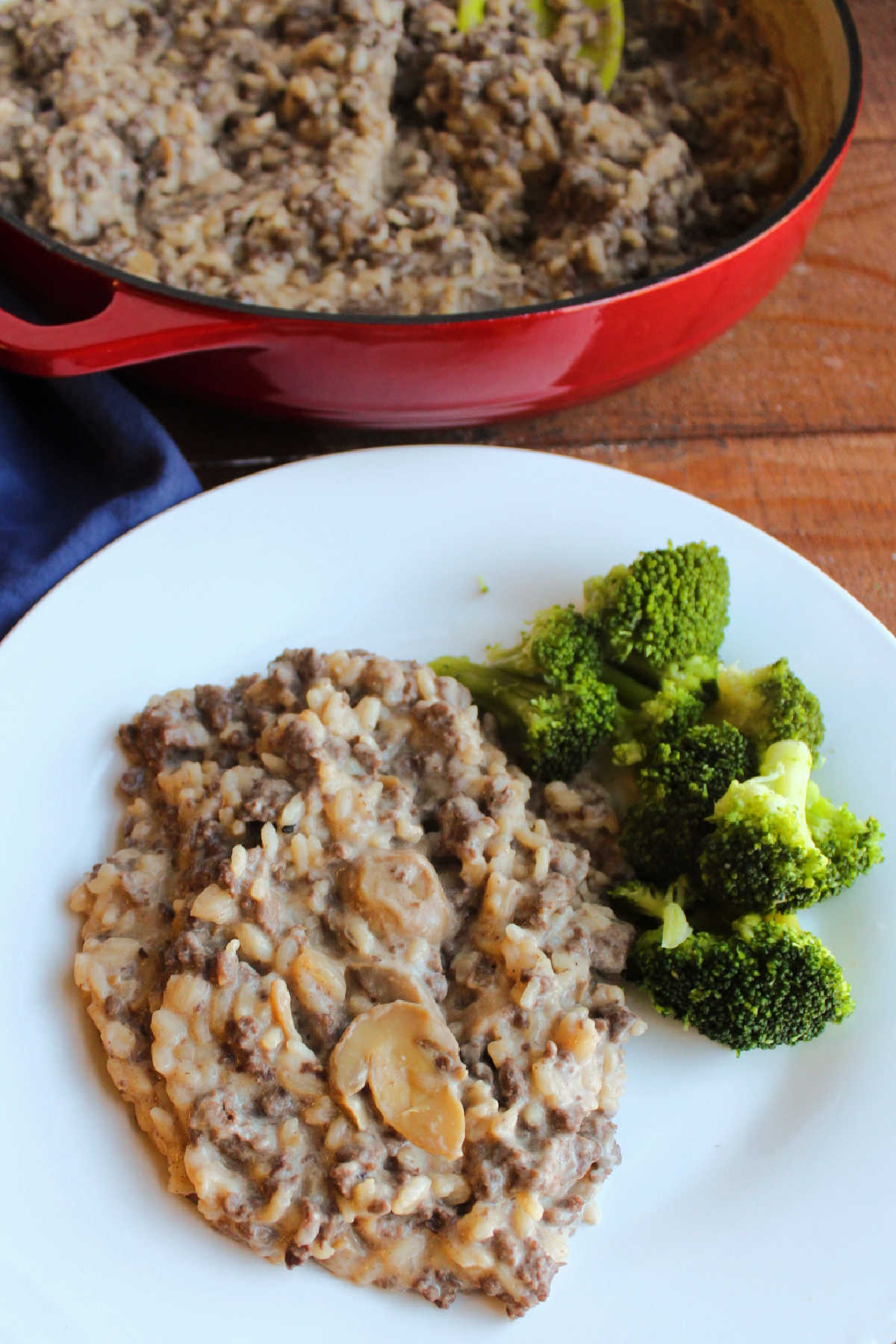 Dinner plate with creamy rice mixture and steamed broccoli with the cast iron pan containing the rest of the rice mixture in the background.