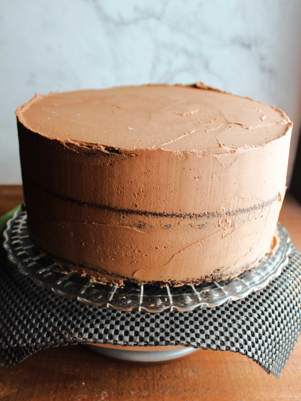 three layers of 10-inch chocolate cake with a crumb coat of chocolate buttercream on it. 