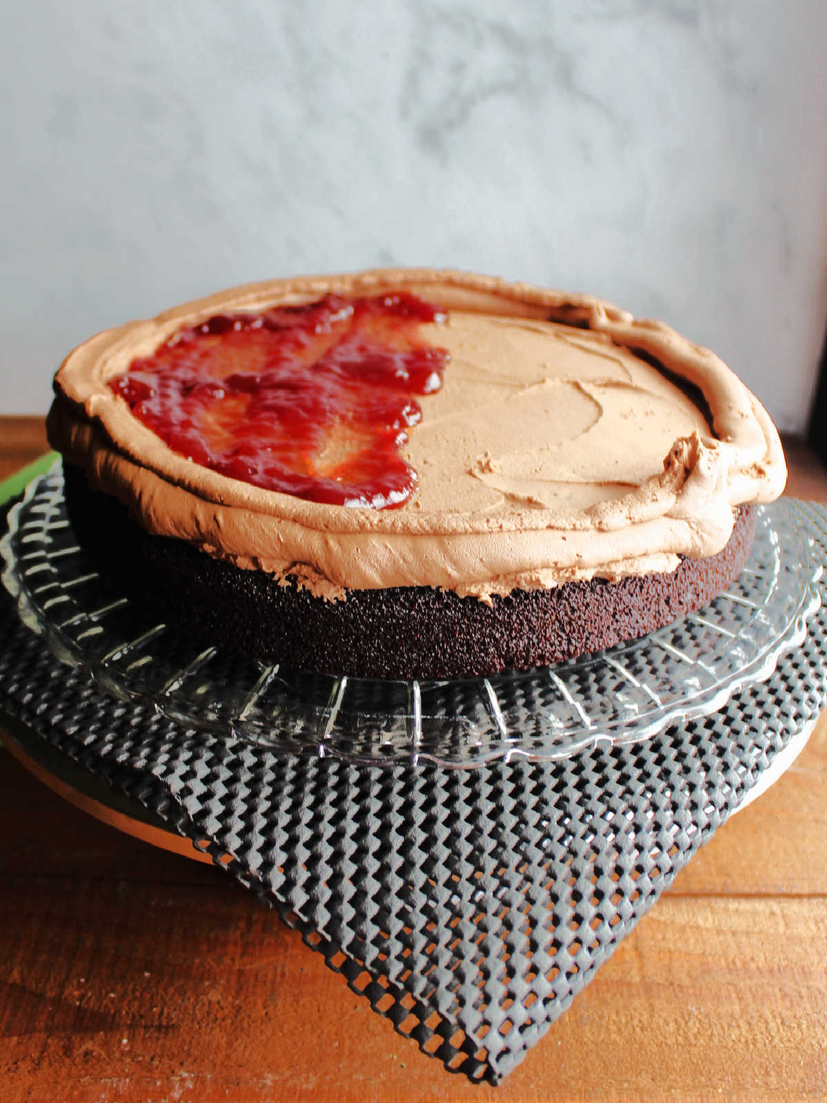 Chocolate cake layer with buttercream spread over the top and a chocolate frosting dam around the edge, starting to spread raspberry filling on the center.