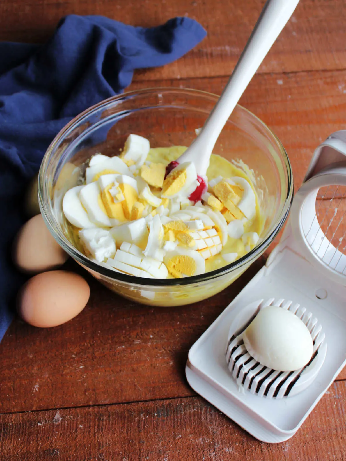 Adding chopped hard boiled eggs to the bowl of dressing mixture.