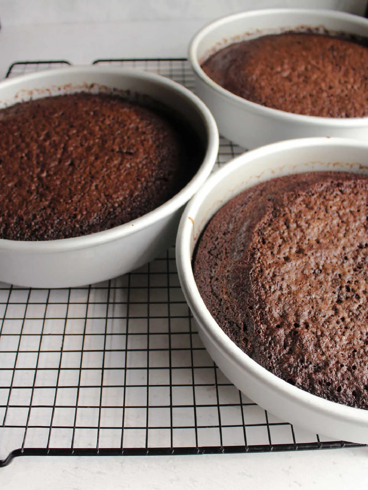 Three 10 inch round chocolate cakes fresh from the oven, cooling on wire rack.