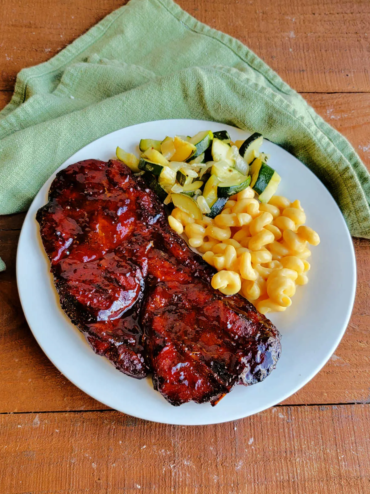 Plate with a large bbq pork steak, macaroni and cheese, and zucchini.