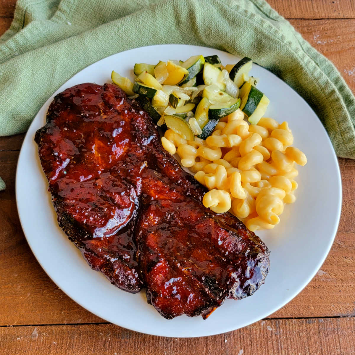 Dinner plate with a glossy bbq pork steak, macaroni and cheese, and sauteed zucchini.