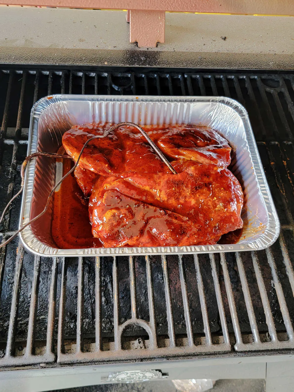 Second step of cooking, the smoked pork steaks are in an aluminum pan with bbq sauce, ready to cook more.