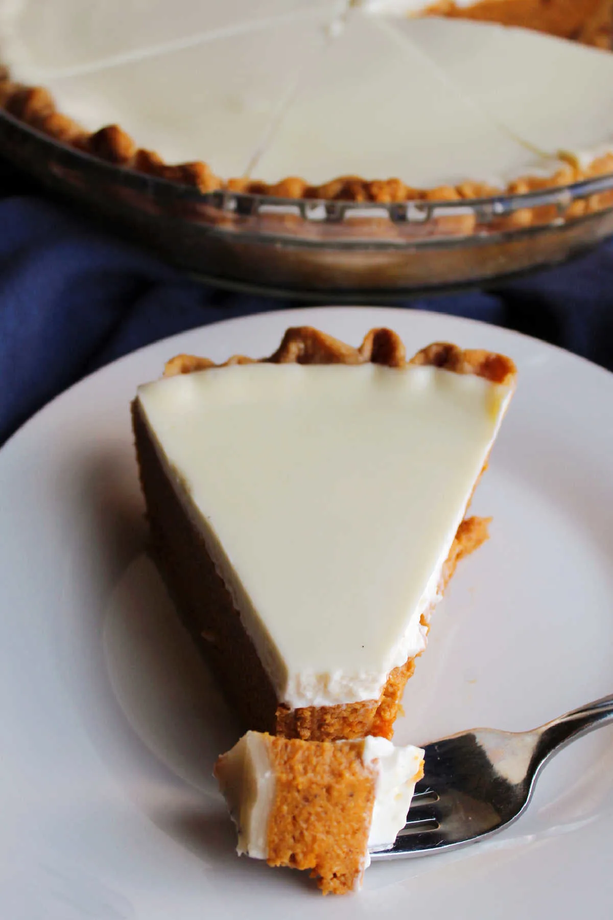 Bite of pumpkin pie on fork laying on plate next to slice of pumpkin pie with smooth sour cream topping covering the top.