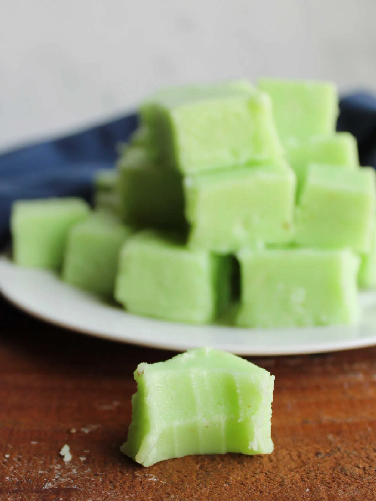 Piece of lime jello fudge with a bite missing, showing creamy texture, with more pieces of fudge in the background.
