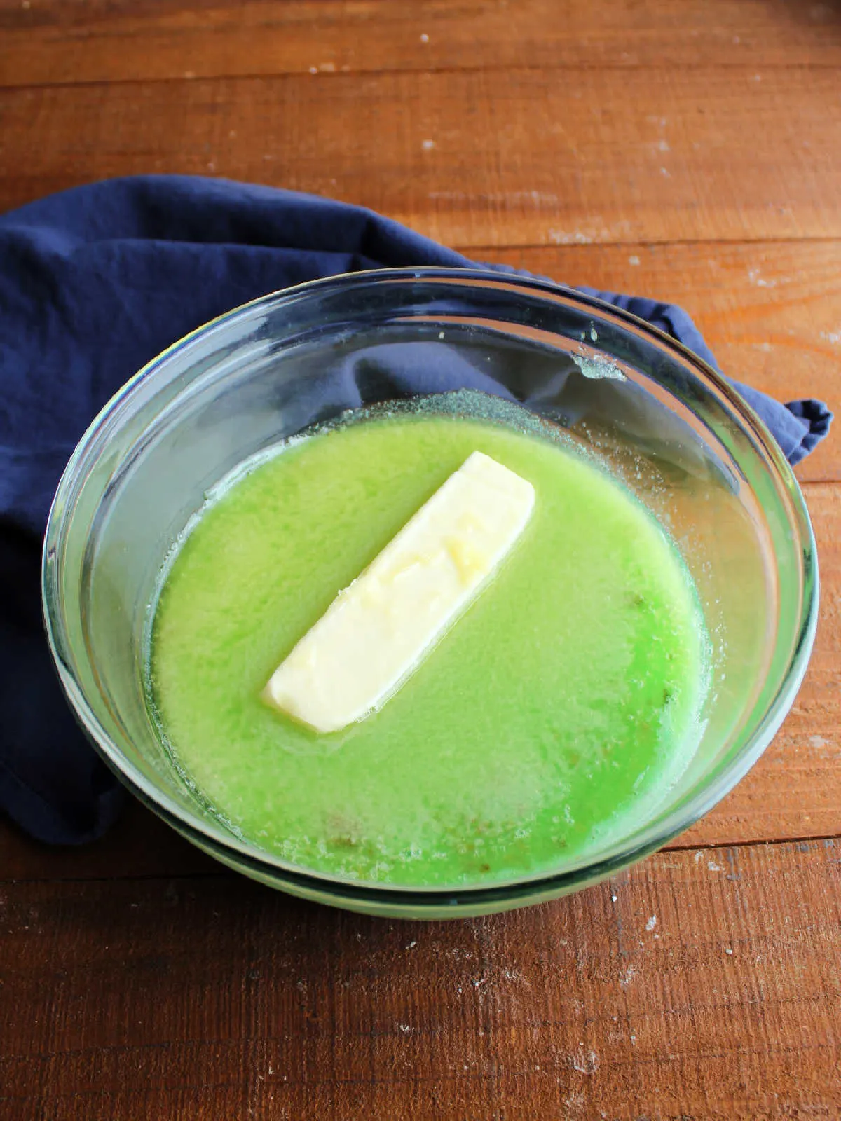 Hot green jello mixture in a bowl with a stick of butter melting inside.