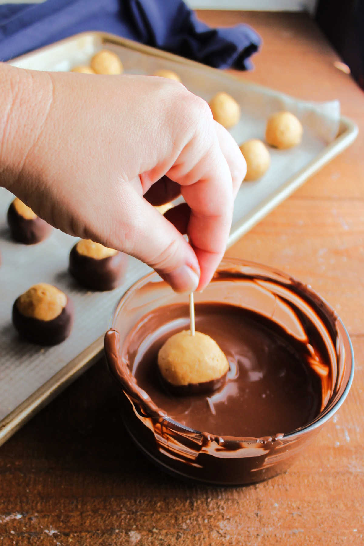 Hand dipping a peanut butter ball in melted dark chocolate using a toothpick to hold the peanut butter center. 