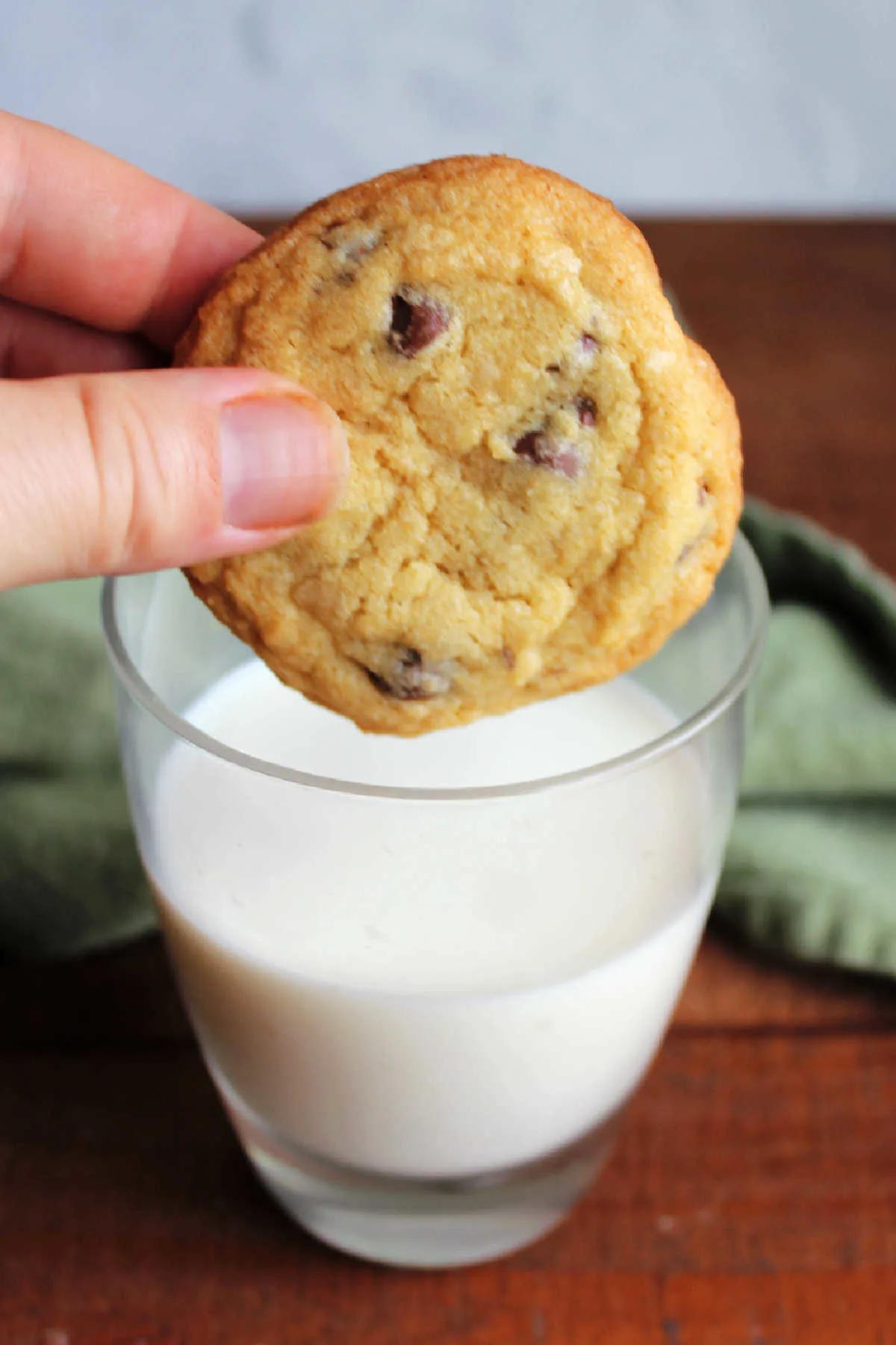 Hand dipping chocolate chip cookie into a glass of milk.