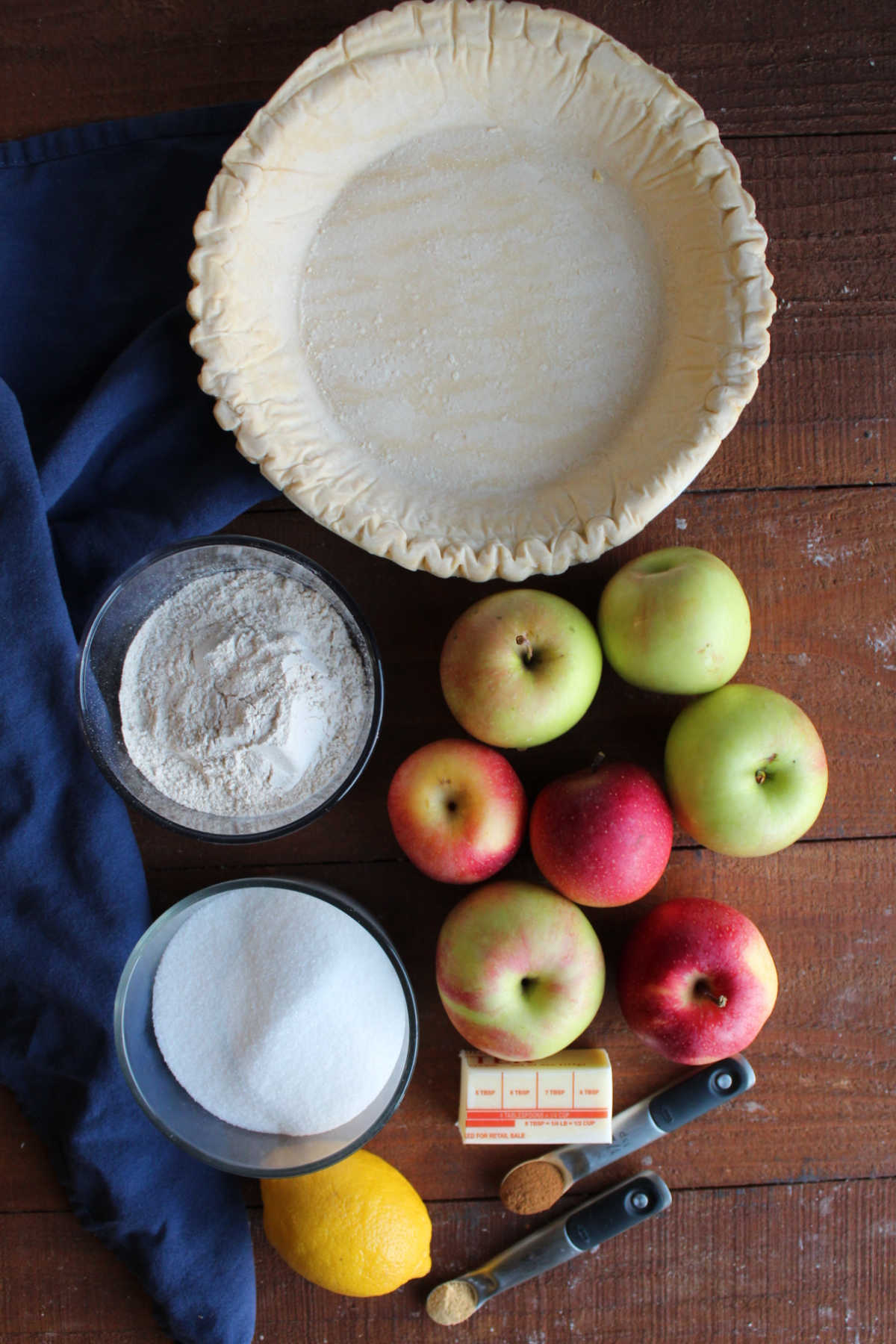 Ingredients including pie crust, apples, butter, cinnamon, ginger, lemon, sugar, and flour ready to be made into a Dutch apple pie.
