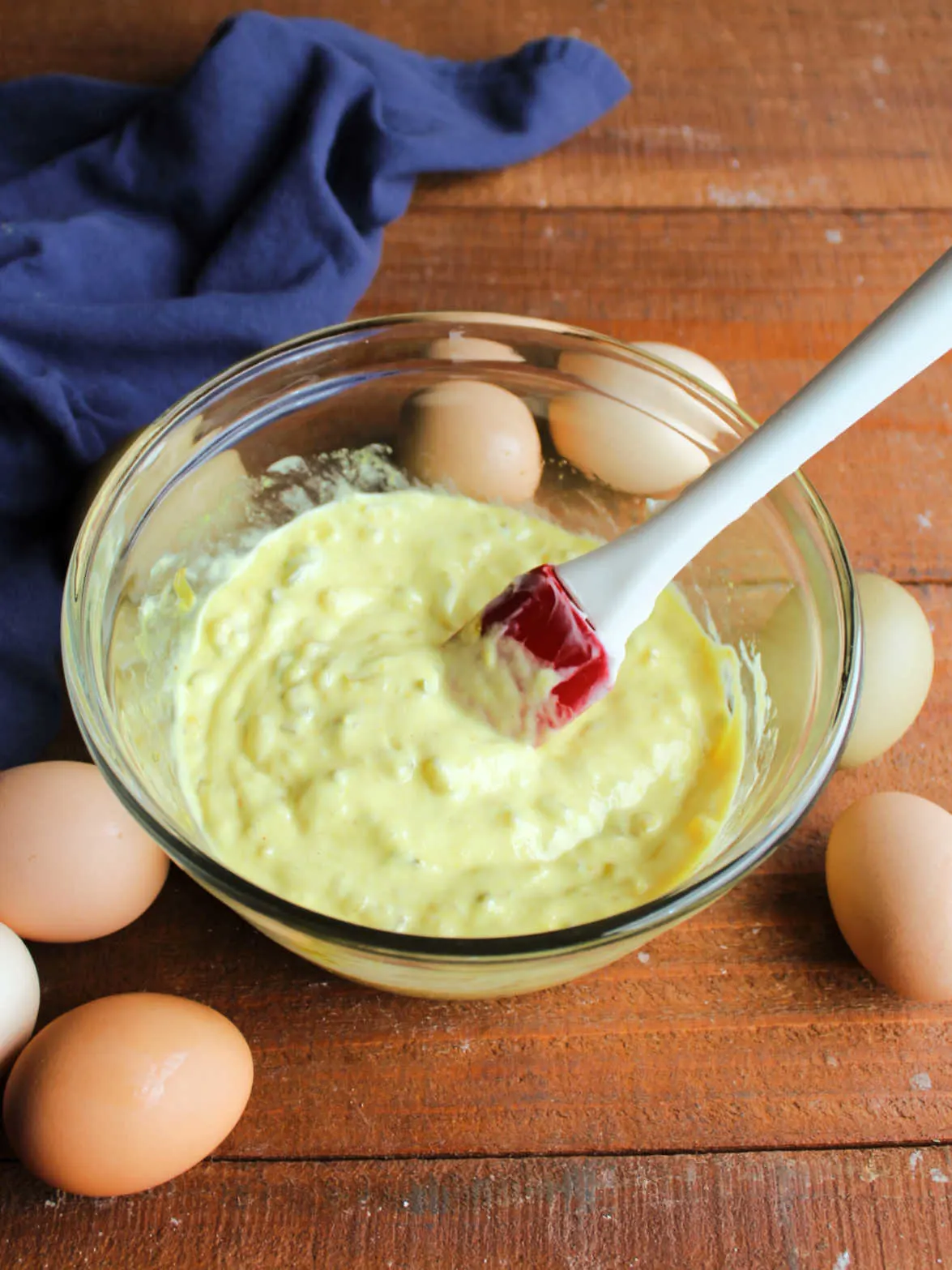 Glass mixing bowl with egg salad dressing mixture made from miracle whip, mustard, and pickle relish.