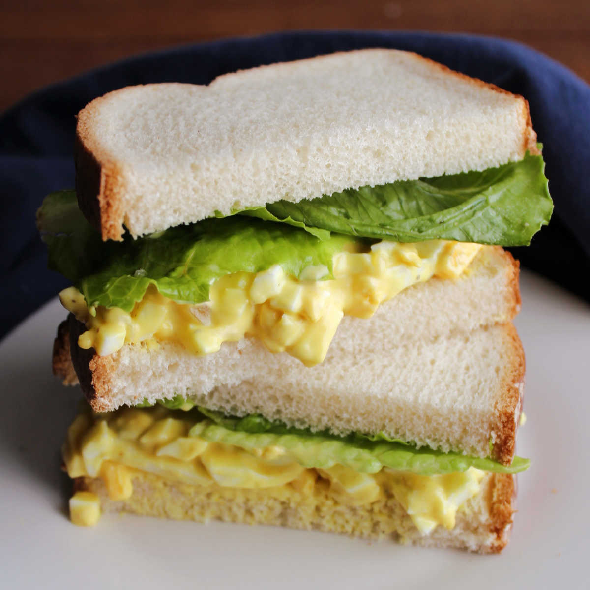Egg salad sandwich with white bread, chunky yellow egg salad, and lettuce cut in half and stacked.