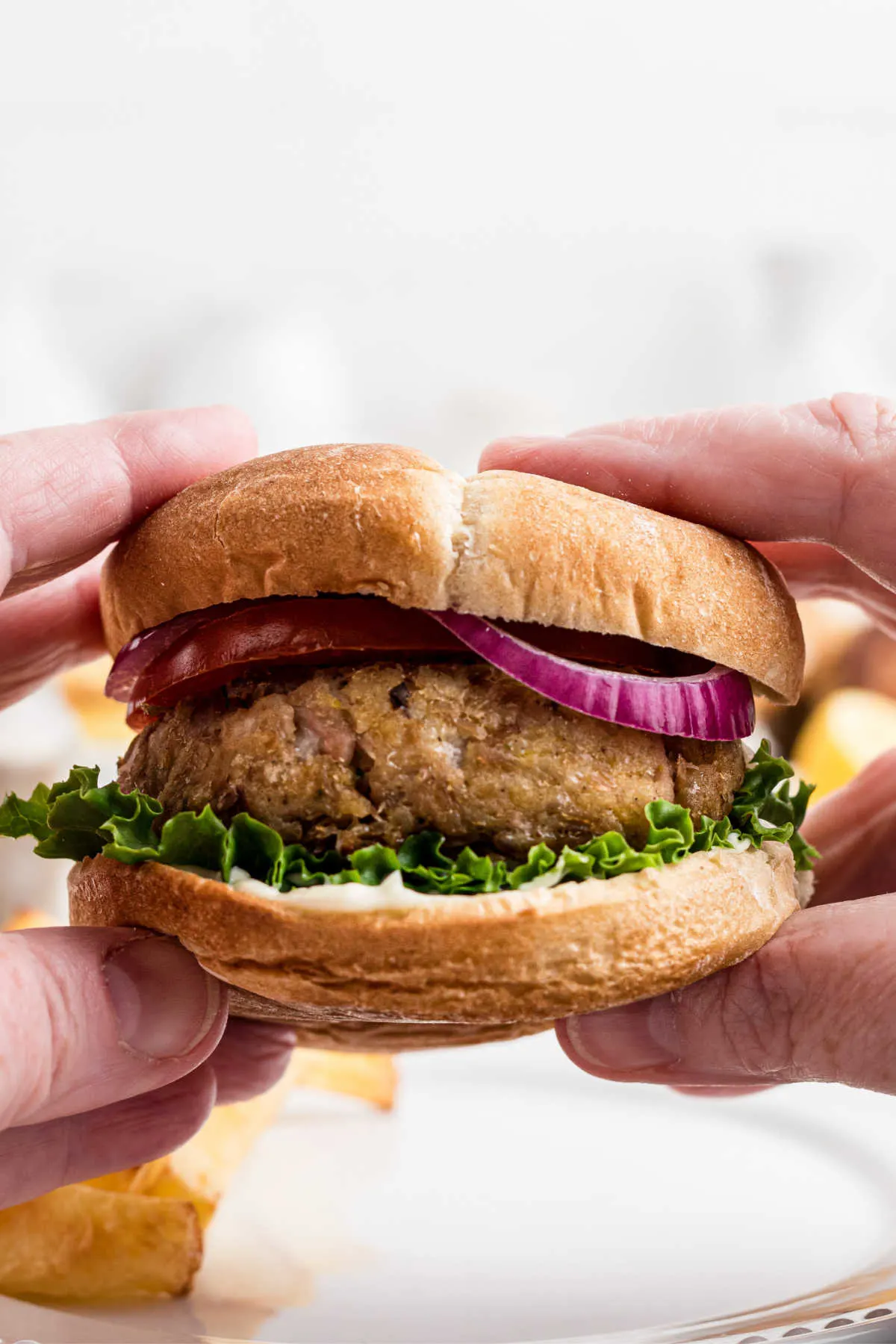 Hands holding tuna burger on bun with lettuce and red onion, ready to eat. 