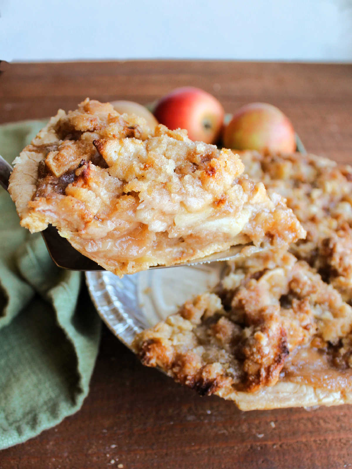 Pie server lifting out a slice of apple crumb pie with soft apple slices in the middle and buttery crumbs on top. 
