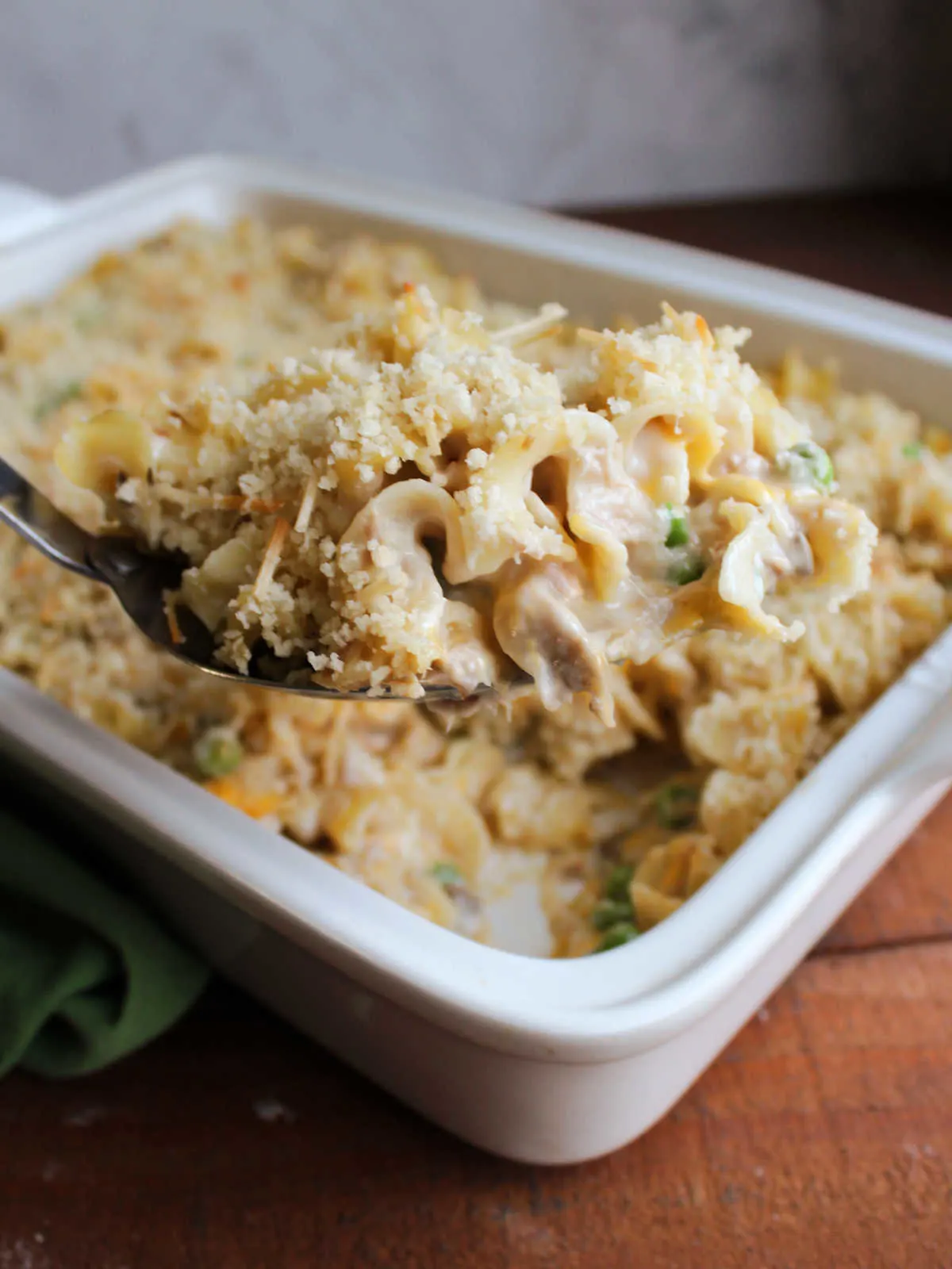 Large serving spoon lifting scoop of tuna noodle casserole out of the pan.