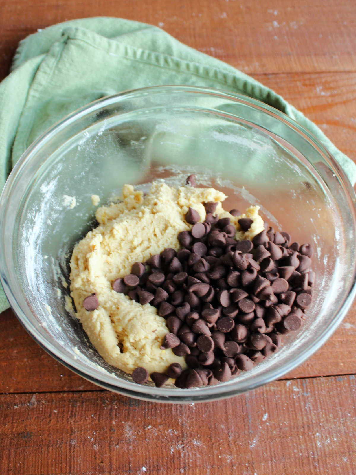 Mixing bowl with cookie dough with pile of chocolate chips ready to be stirred in.