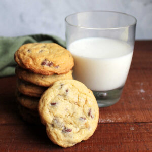 Stack of chewy chocolate chip cookies next to glass of milk.