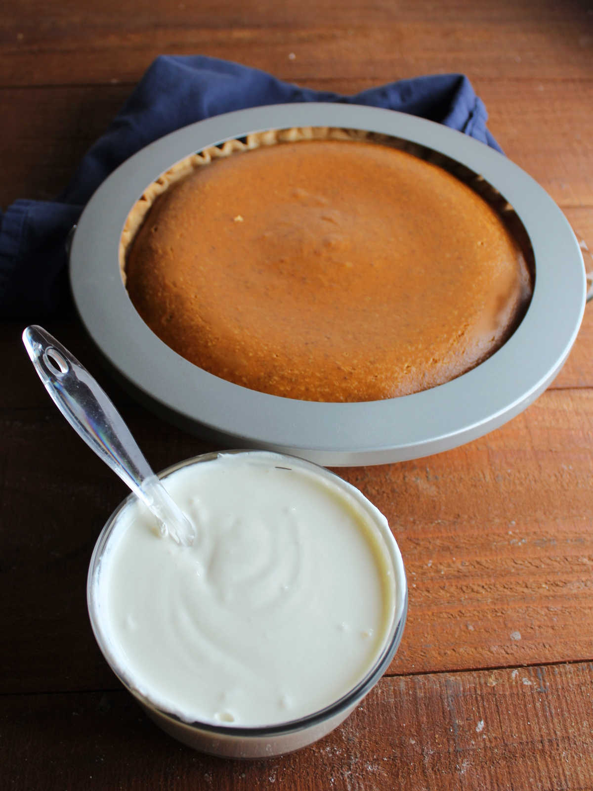 Small bowl of sour cream, sugar, and vanilla mixture in front of a mostly baked pumpkin pie.