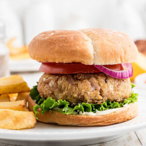 Tuna burger on bun with red onion and lettuce served with french fries.