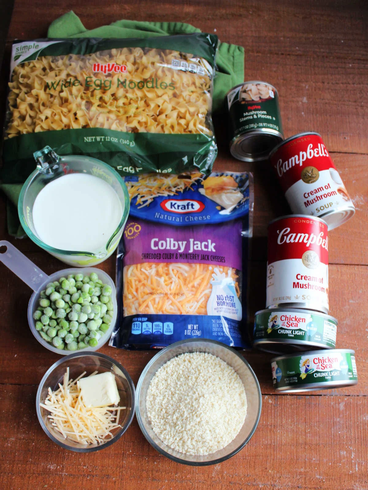 Ingredients including egg noodles, cream of mushroom soup, tuna, cheese, bread crumbs, butter, Parmesan, peas, and milk. 