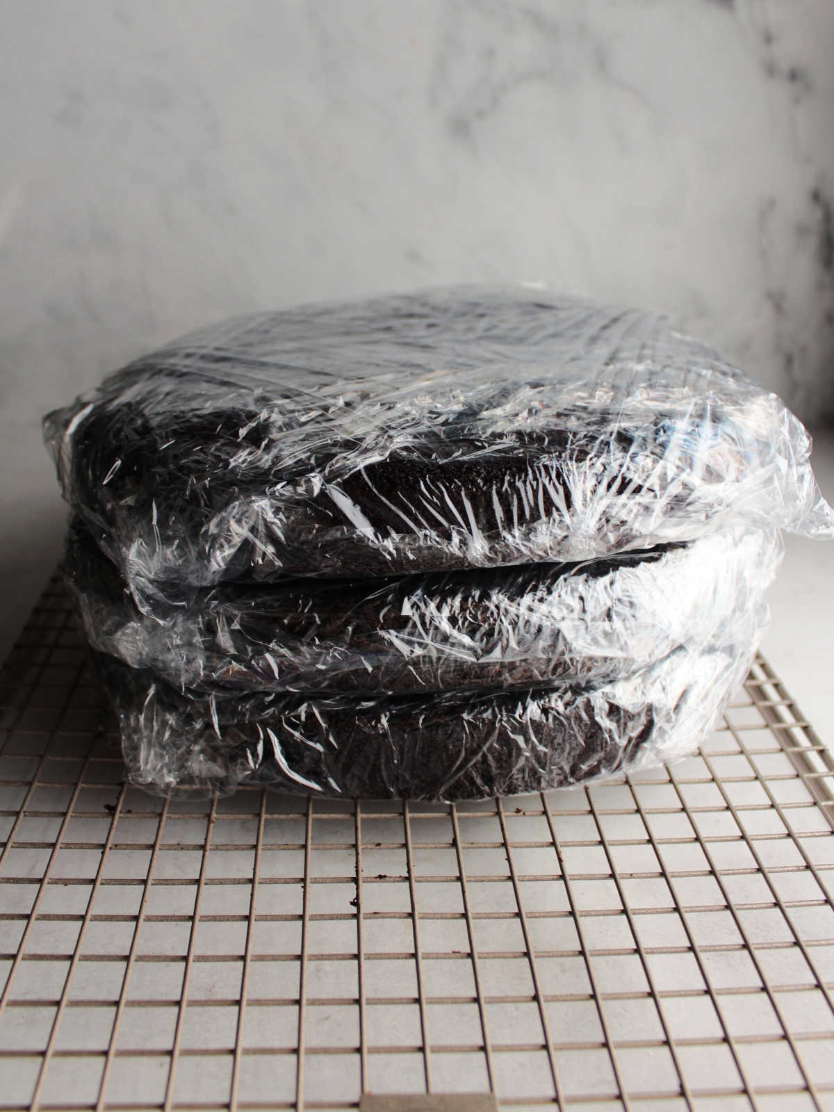Three chocolate cake layers wrapped in plastic wrap, ready to go in the freezer.