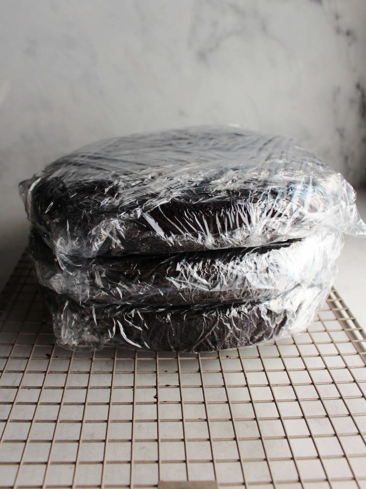 Three chocolate cake layers wrapped in plastic wrap, ready to go in the freezer.