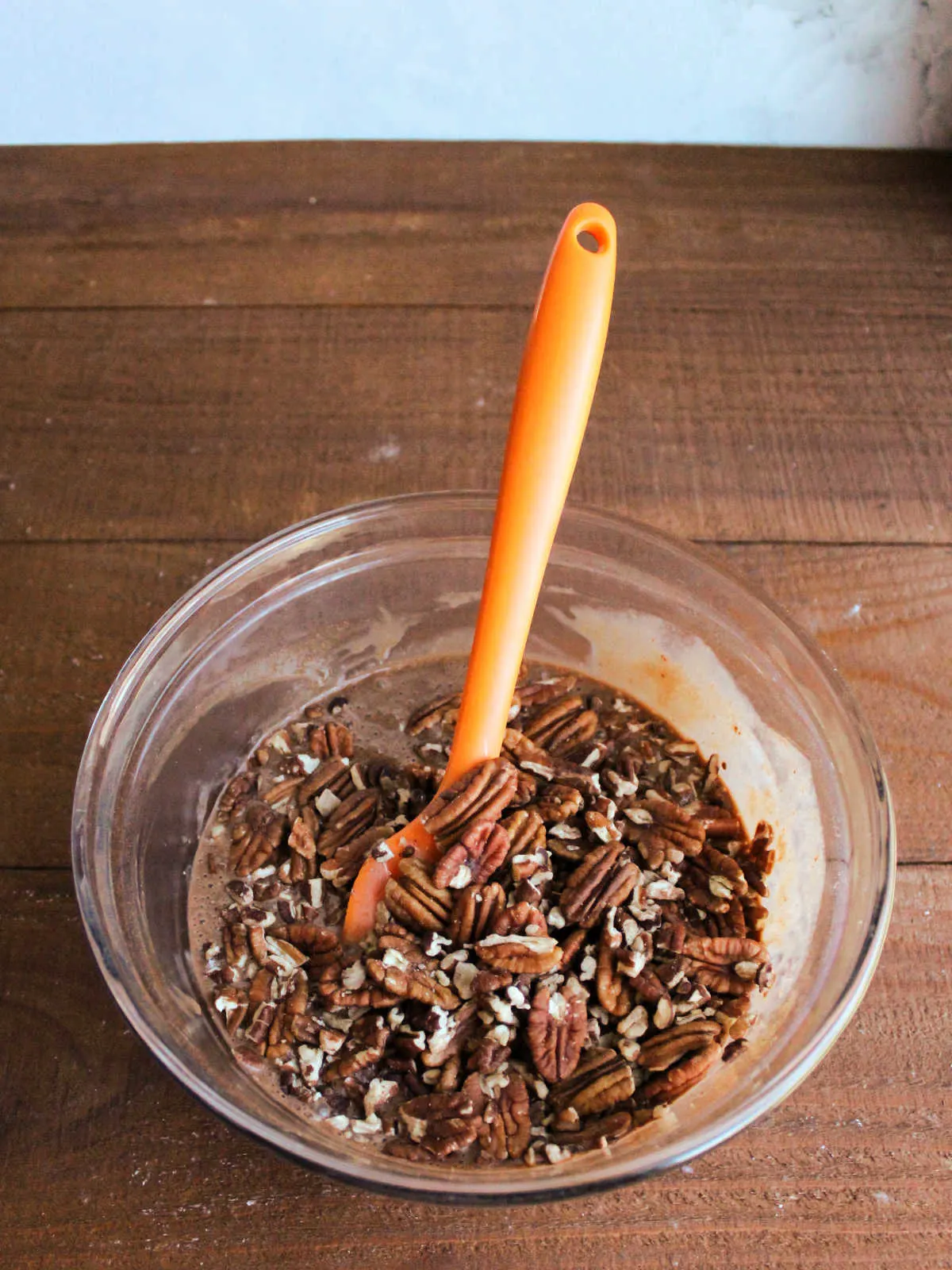 Mixing bowl of chocolate condensed milk filling mixture topped with toasted pecans, ready to be stirred together.