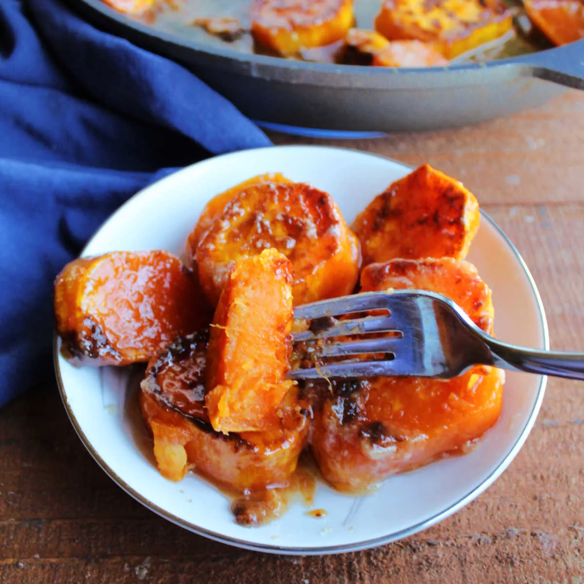 Bite of skillet sweet potato of fork showing soft orange interior and sticky caramelized exterior.