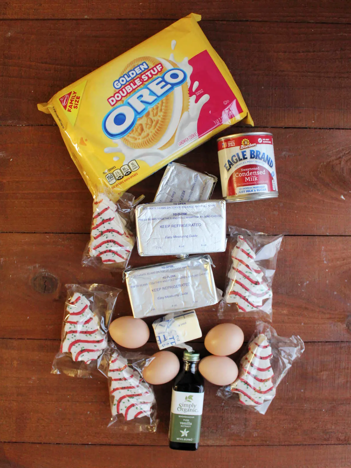 Ingredients including vanilla Oreos, sweetened condensed milk, cream cheese, eggs, vanilla, and Little Debbie Christmas tree snack cakes ready to be made into a cheesecake.