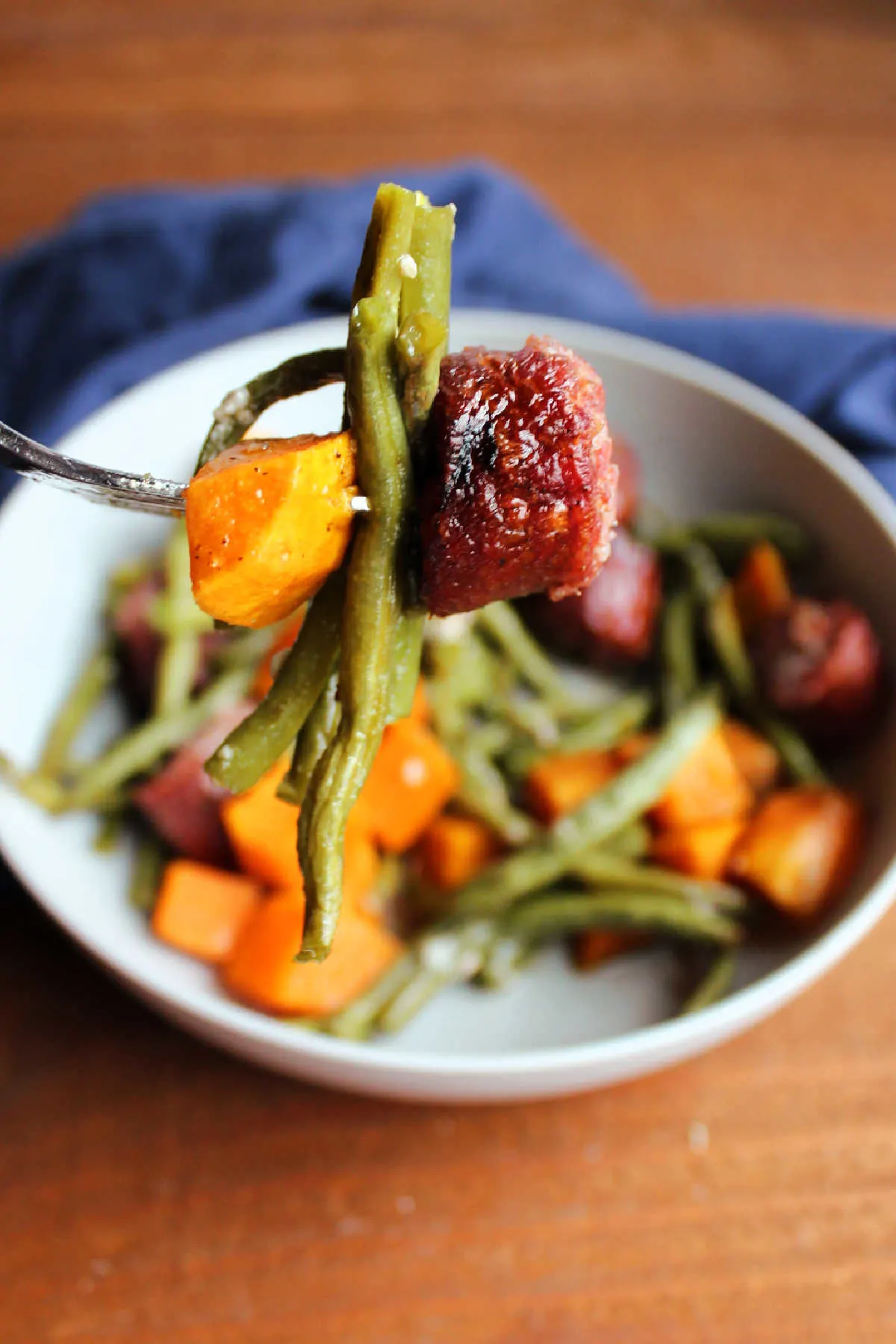 Bite of kielbasa, green beans and chunk of sweet potato on fork, showing roasted texture of each.
