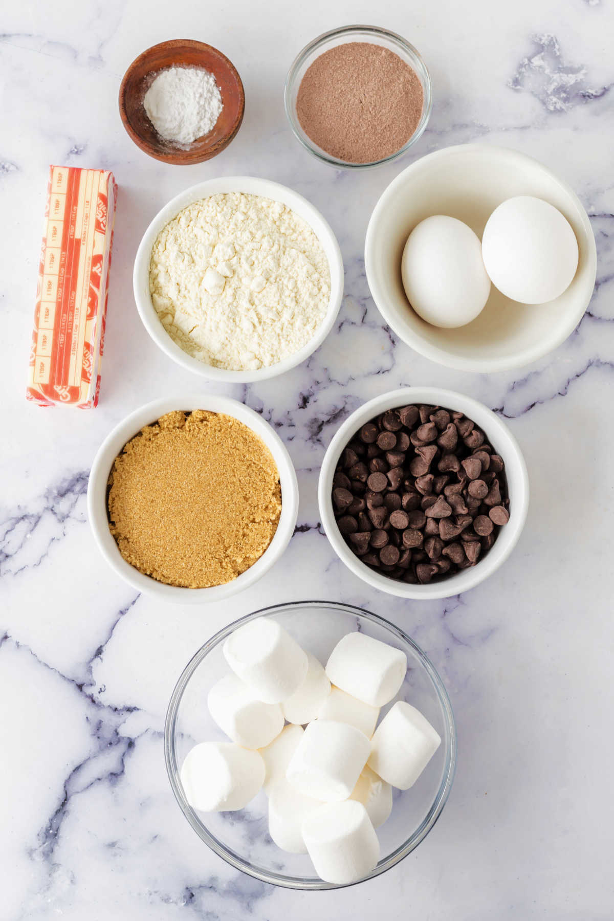 Ingredients including butter, chocolate chips, brown sugar, flour, eggs, hot cocoa mix, baking powder, and marshmallows ready to be made into hot chocolate cookies.