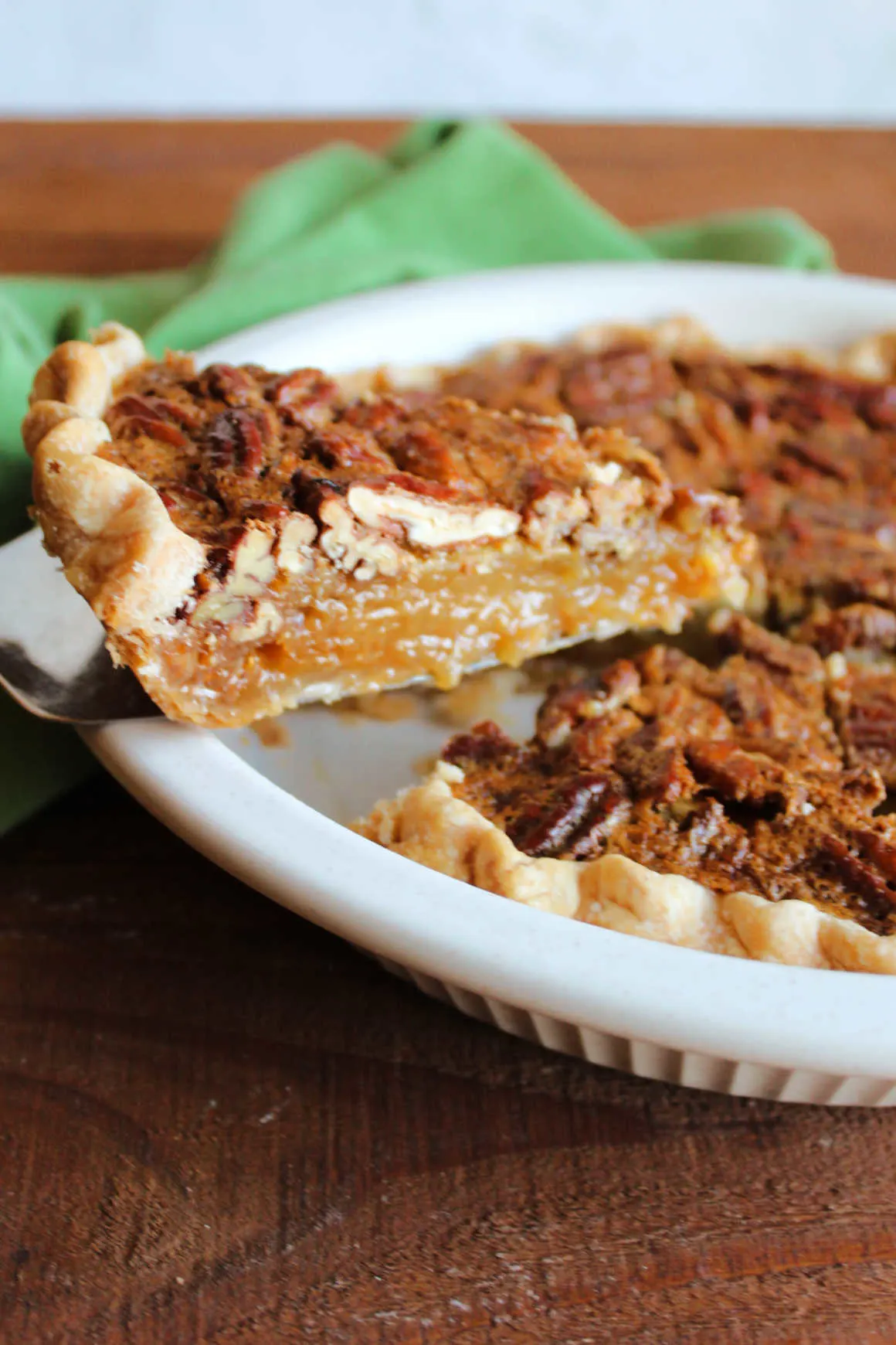 Pie serving lifting out slice of classic pecan pie with gooey filling and lots of rich pecans on top.