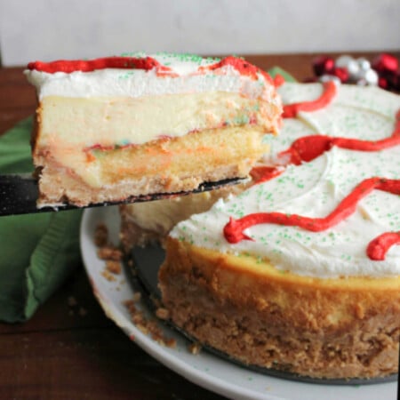 Lifting first slice of Little Debbie Christmas tree cheesecake out showing layer of crust topped with cake, then cheesecake and marshmallow buttercream for layers of festive goodness.