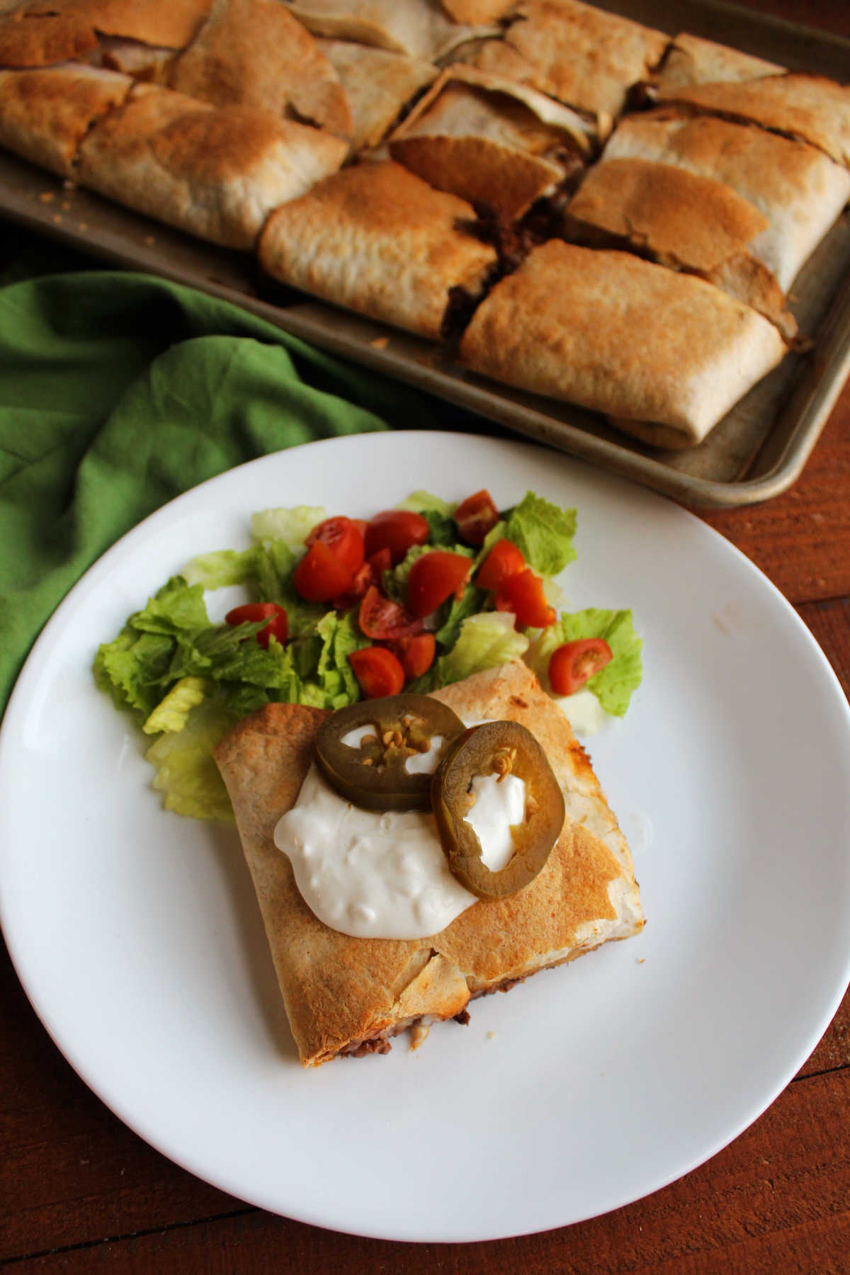 Piece of baked quesadilla topped with sour cream and jalapenos and served with shredded lettuce and diced tomatoes.