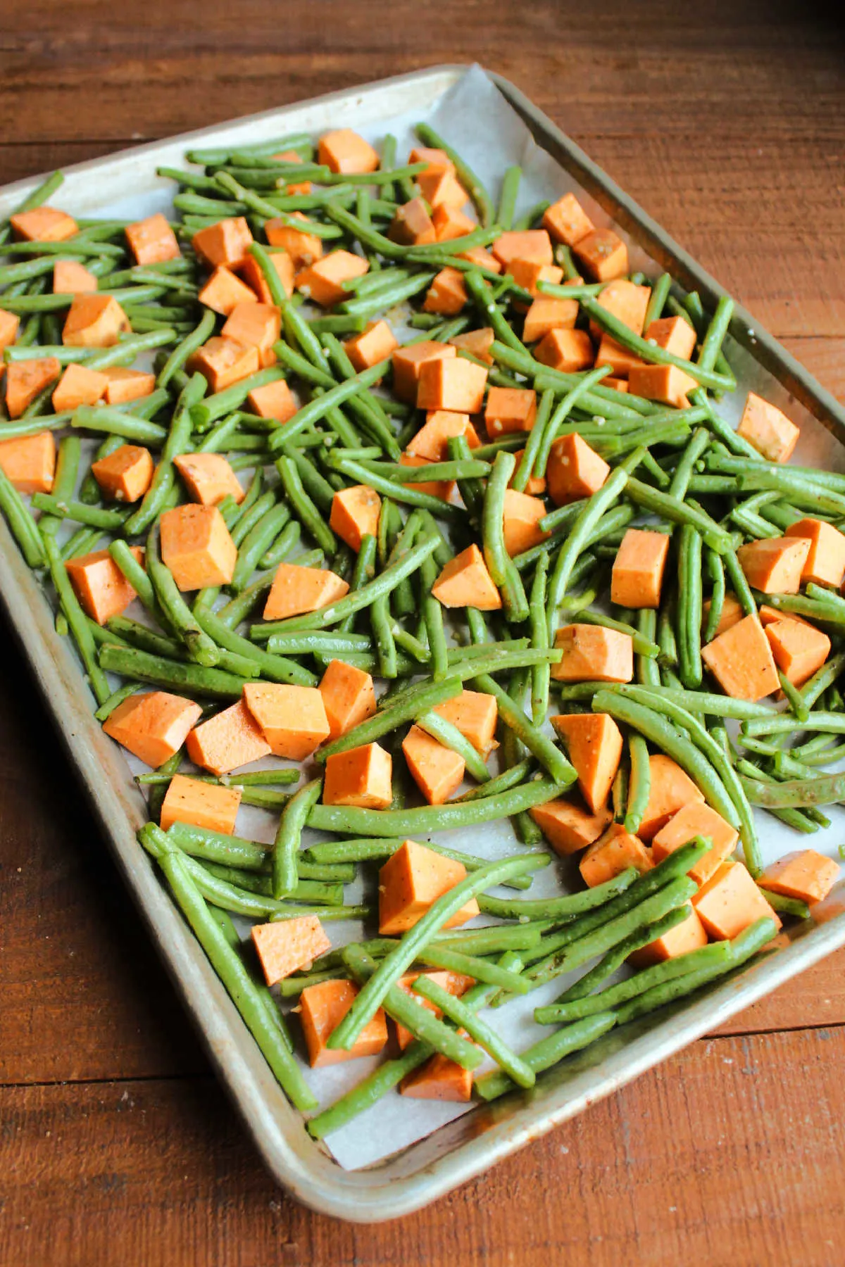 Trimmed green beans and sweet potato chunks tossed in oil and seasonings on sheet pan.
