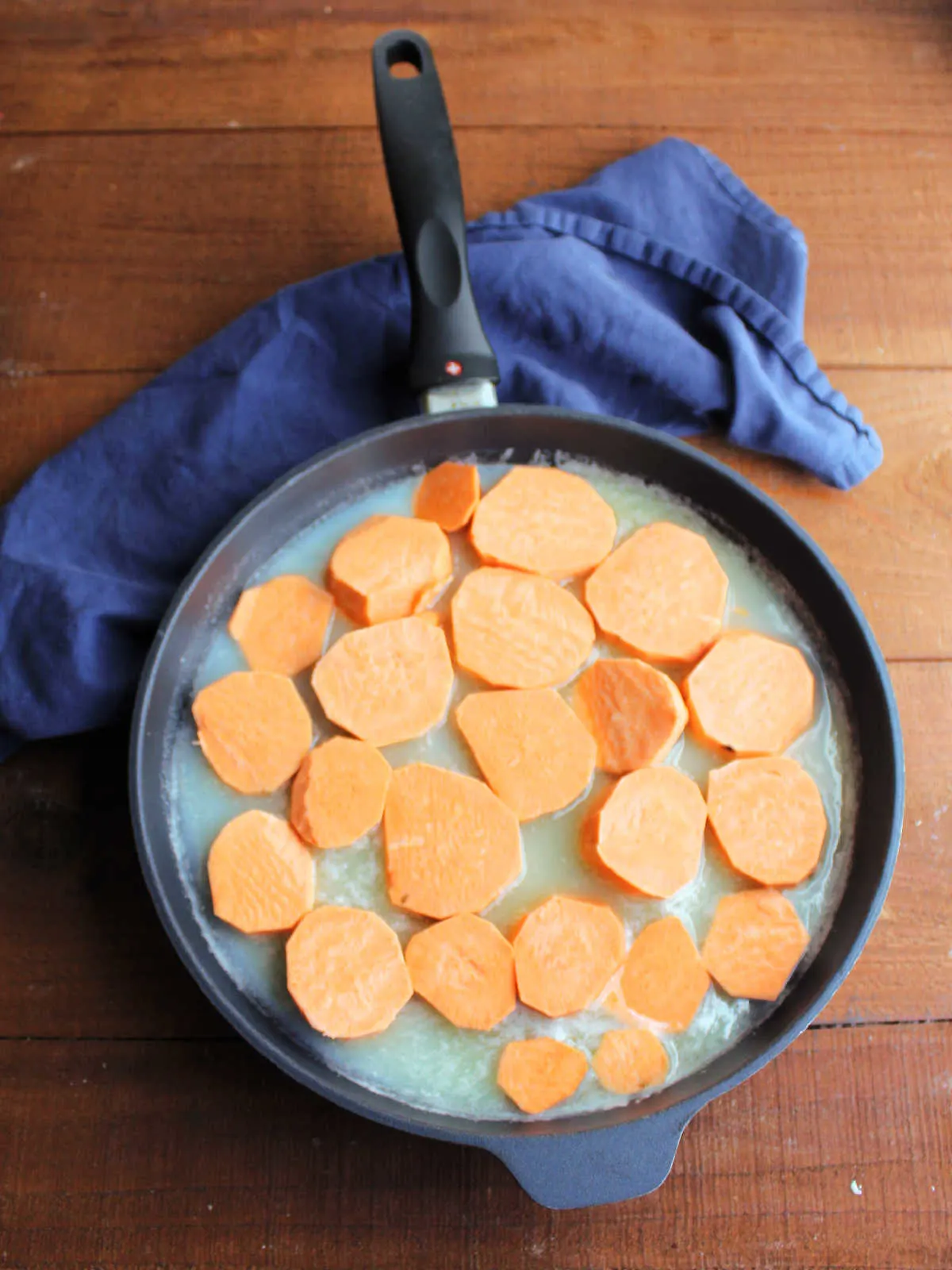 Thick slices of sweet potato in skillet with syrup, ready to cook.