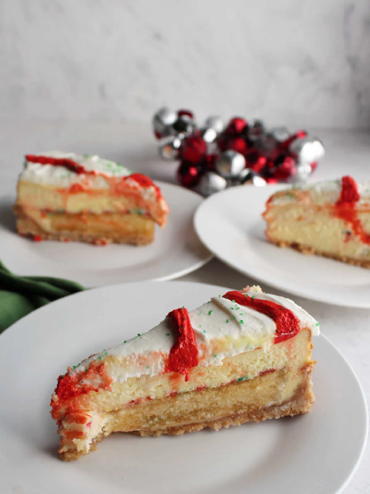 Three slices of Little Debbie christmas tree cheesecake served on small plates showing the layers of crust, cake, cheesecake, and frosting.