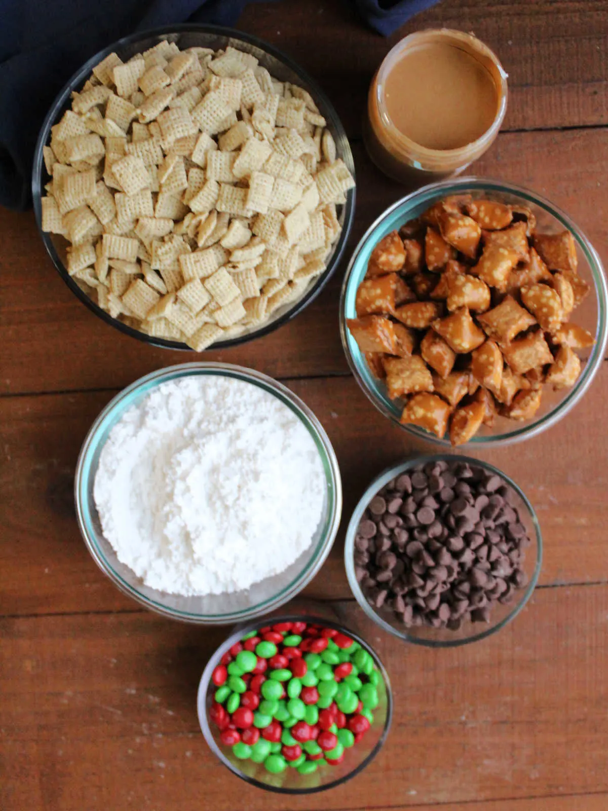 Ingredients including Chex cereal, peanut butter, peanut butter filled pretzels, chocolate chips, holiday M&Ms and powdered sugar. 